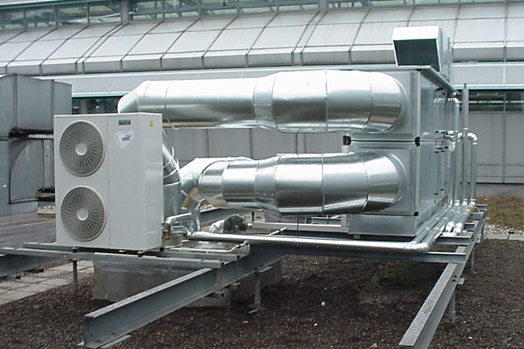 Lüftungs- und Klimaanlage auf einem Flachdach mit großen Metallrohren und Außengerät zur Luftführung und Klimatisierung eines Gebäudes.
