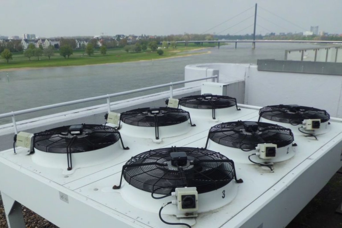 Große Klimaanlage mit mehreren Ventilatoren auf einem Flachdach, Blick auf den Rhein und eine Brücke im Hintergrund.